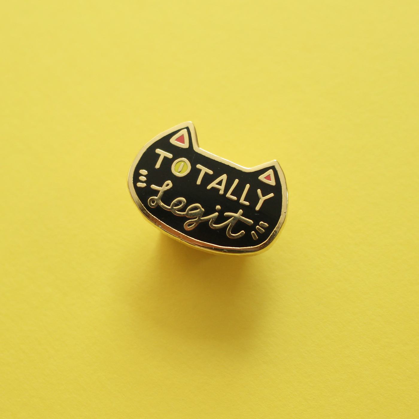 The Totally Legit pin photographed flat on a yellow background