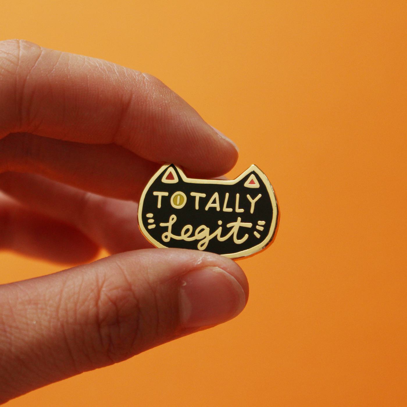 The pin held between finger and thumb against an orange background, for scale