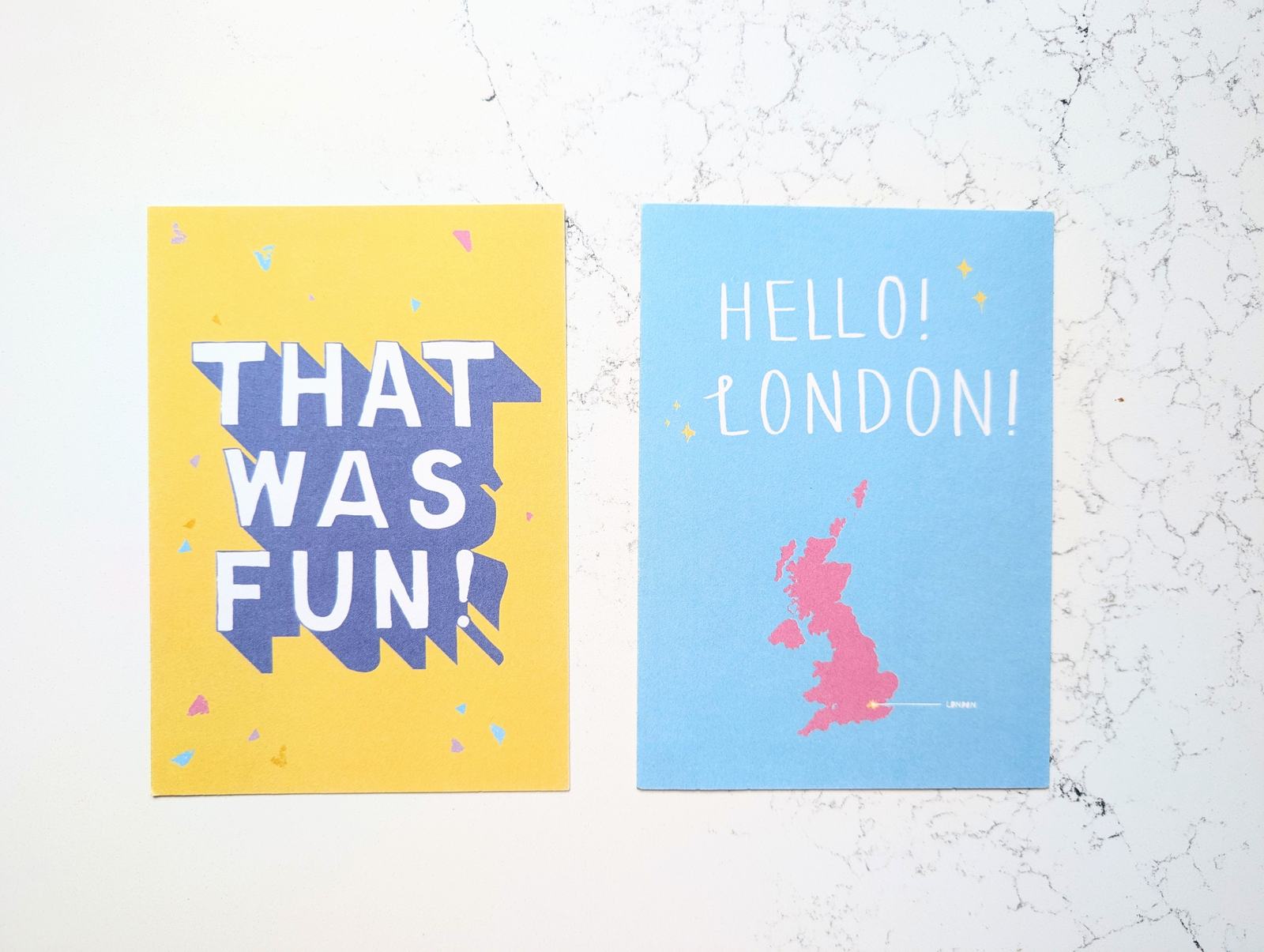 Two postcards: THAT WAS FUN! in blue block letters on yellow, and HELLO! LONDON! above a pink map of Britain
