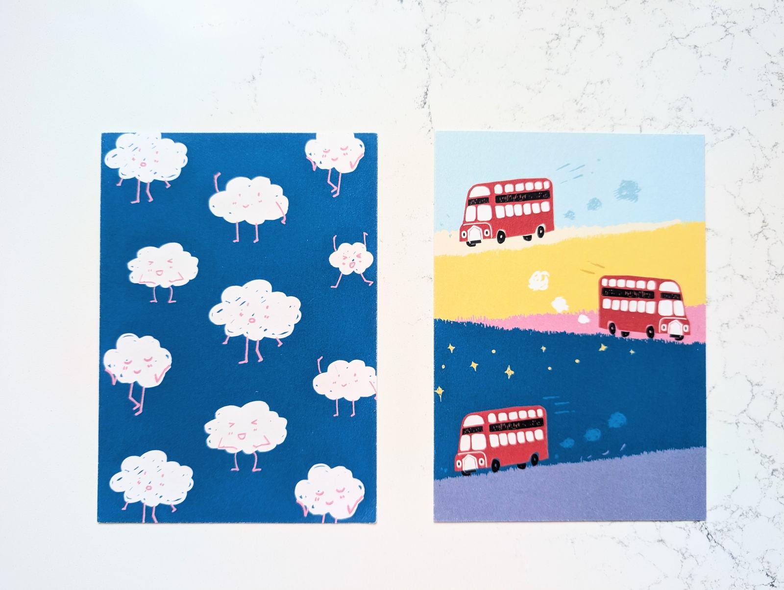 Two postcards: clouds with legs walking across navy, and red double-decker buses on bands of yellow, pink and purple